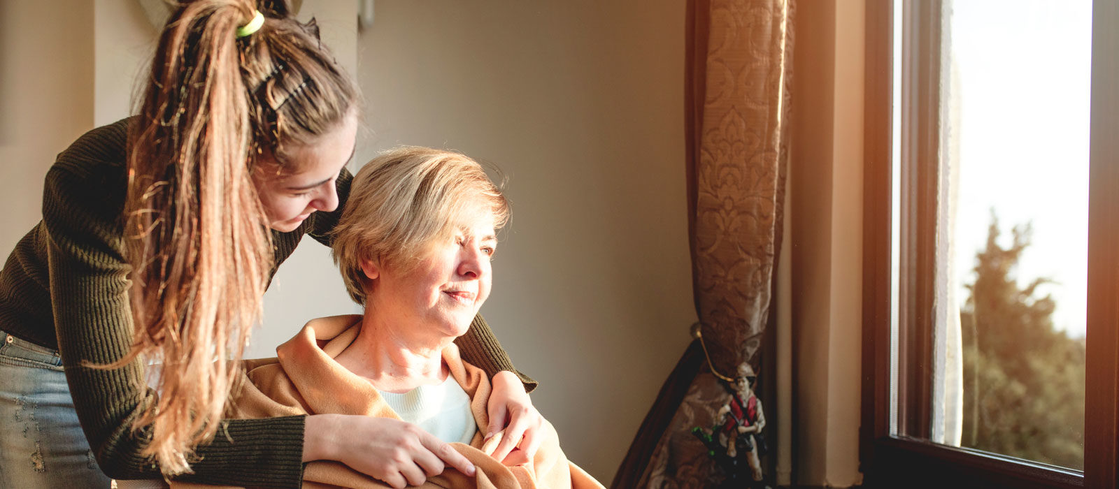 Daughter hugging mother as she looks outside window