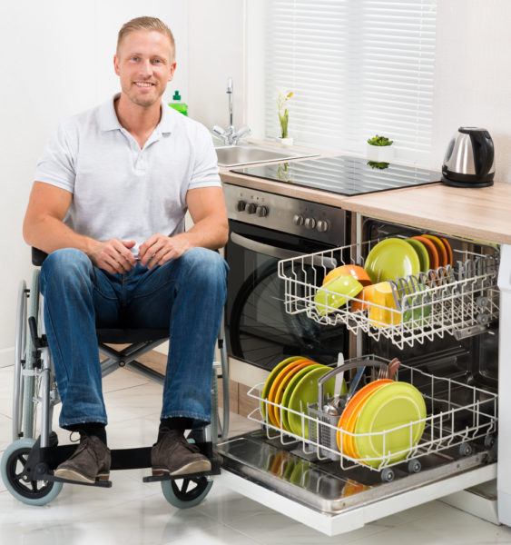 man sitting in a wheelchair while loading the dishwasher